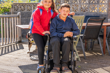 2 young people, one is in a wheelchair.  The other is standing behind helping